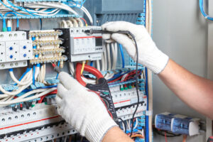 The senior electrician with a diagnostic tool in his hand, standing next to the electrical panel, measures the performance of electrical circuits.